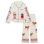 A two-piece Big Folk pajama set featuring a long-sleeve button-front top and matching pants in an off-white fabric. The pajamas are decorated with red and multicolor festive illustrations, including a Santa Claus figure, a reindeer, and Nordic-style patterns with text labels.