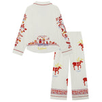 The back of a two-piece Big Folk pajama set shown flat on a white background, featuring a long-sleeve top and matching pants. The pajamas are off-white with festive red, yellow, and blue illustrations of reindeer, snowflakes, and a Christmas village scene, with the brand name Lapland visible on the back by the bottom seem of the top.