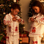 Two children wearing matching Small Folk pajamas standing in front of a decorated Christmas tree in a warmly lit room.