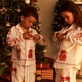 Two children wearing matching Small Folk pajamas standing in front of a decorated Christmas tree in a warmly lit room.