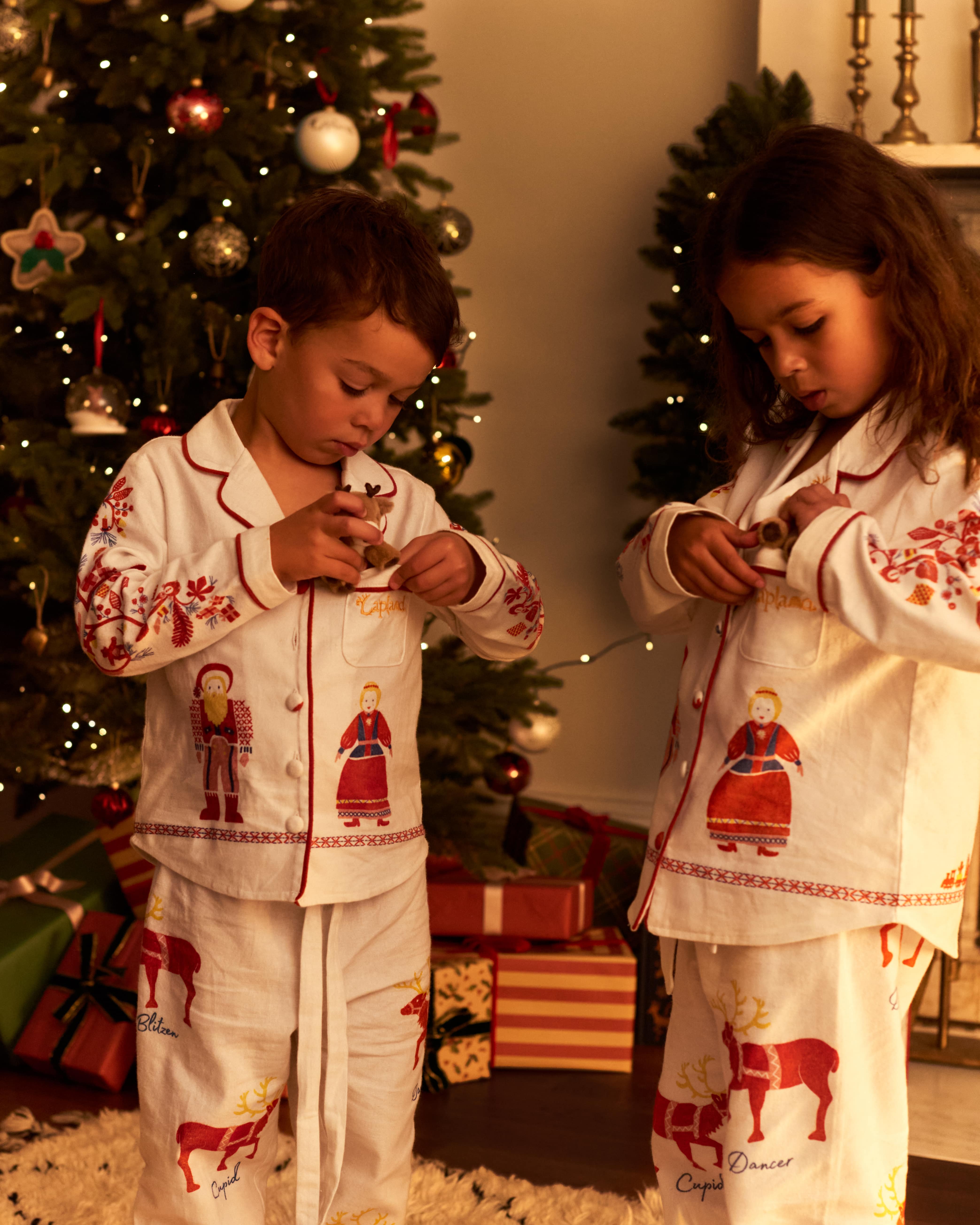 Two children wearing matching Small Folk pajamas standing in front of a decorated Christmas tree in a warmly lit room.