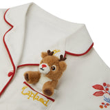 Close-up of a Small Folk Pyjamas top, with red trim, featuring a small plush brown reindeer attached near the chest pocket area and embroidered red floral details on the lower right.