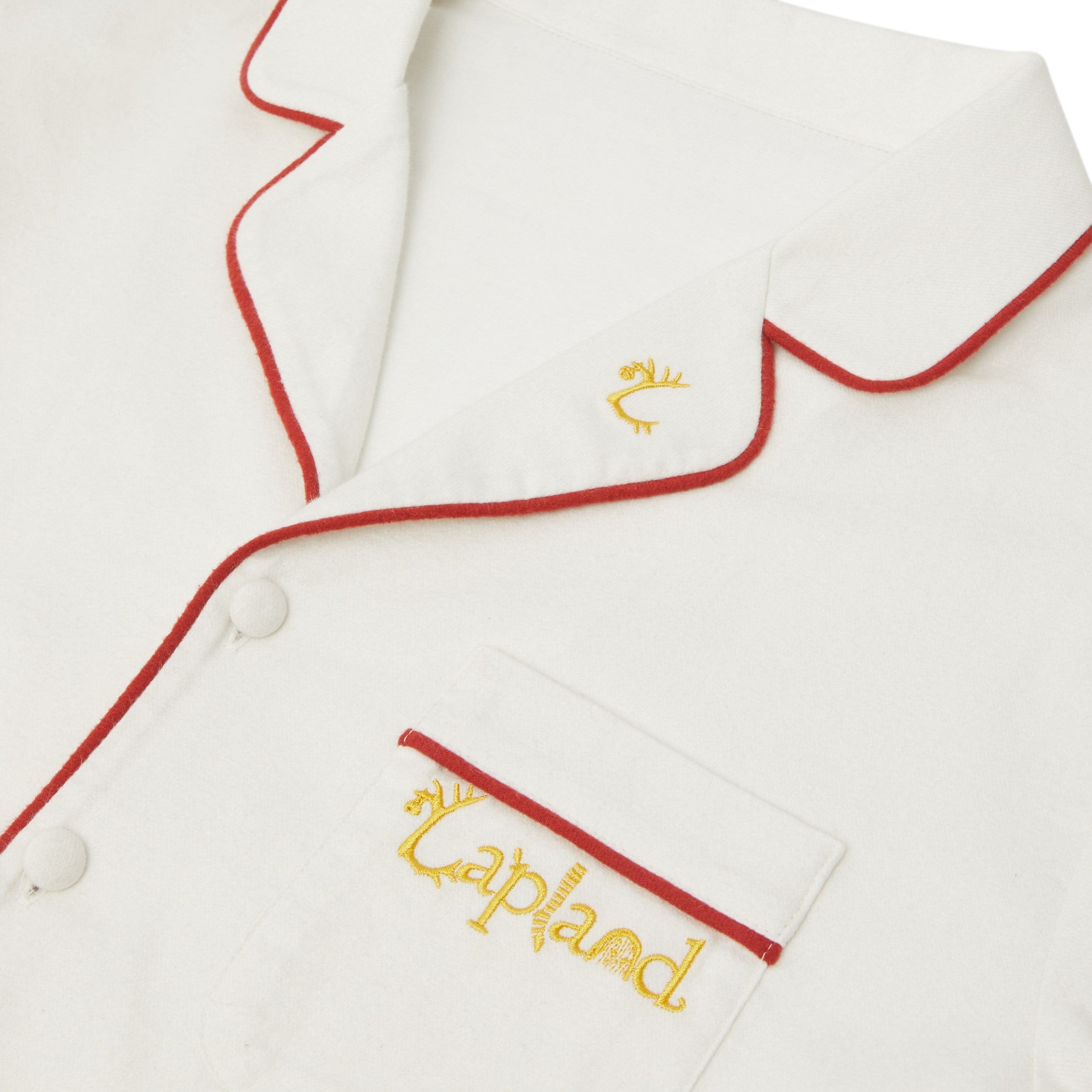 Close-up of a Big Folk pyjama top with red piping trim and yellow embroidered text reading 'Lapland' on the chest pocket.
